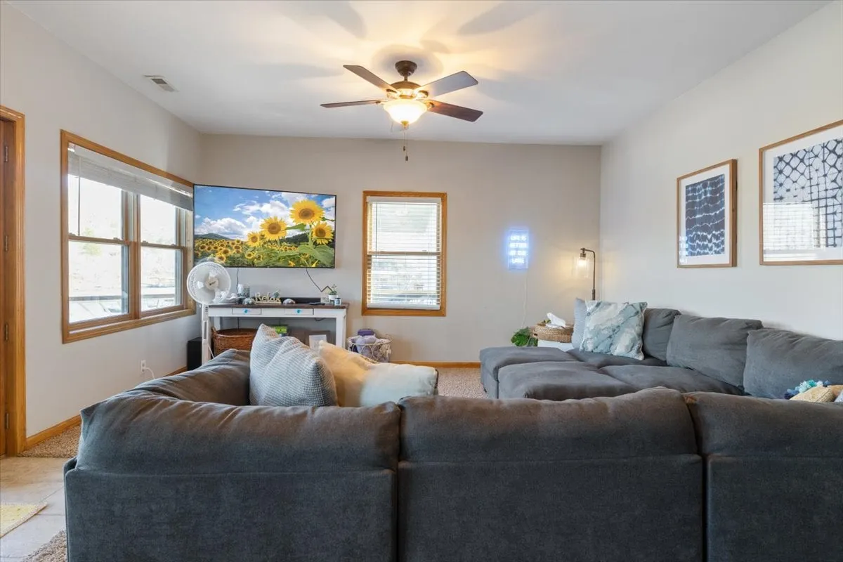 A welcoming living room with a large sectional sofa, wall-mounted TV displaying a sunflower image, decorative art, and an abundance of natural light streaming through the windows. The arrangement encourages group activities and fosters togetherness.