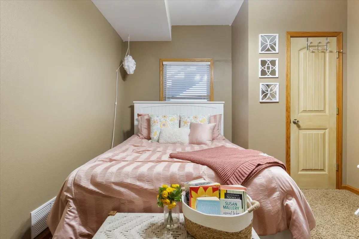A warmly lit bedroom featuring a plush bed adorned with decorative pillows, a bedside table with books and flowers, and an inviting reading nook. The cozy setting highlights the restful atmosphere intended for guests.