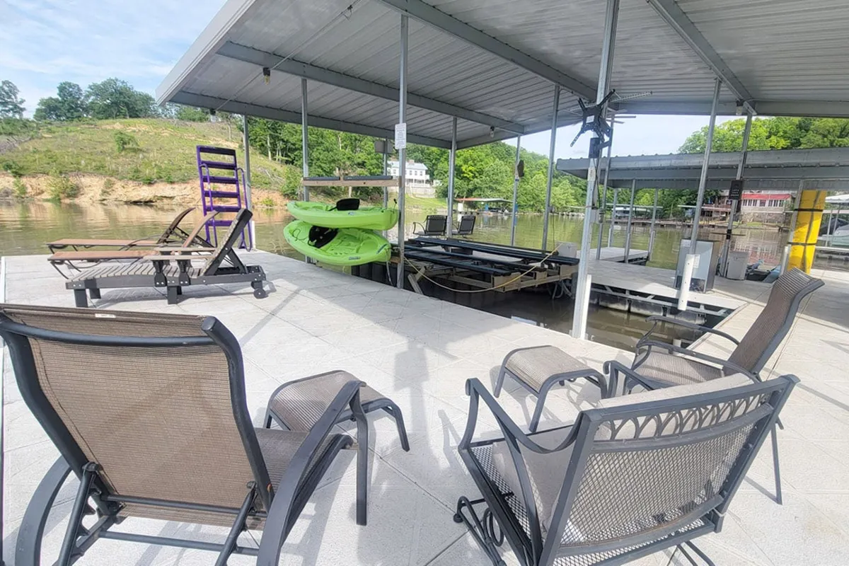 A peaceful dockside scene features a kayak, lawn chairs, and a tranquil stretch of lake. The setting is framed for relaxation, sunbathing, fishing, or launching into water adventures, with the dock area beckoning exploration.