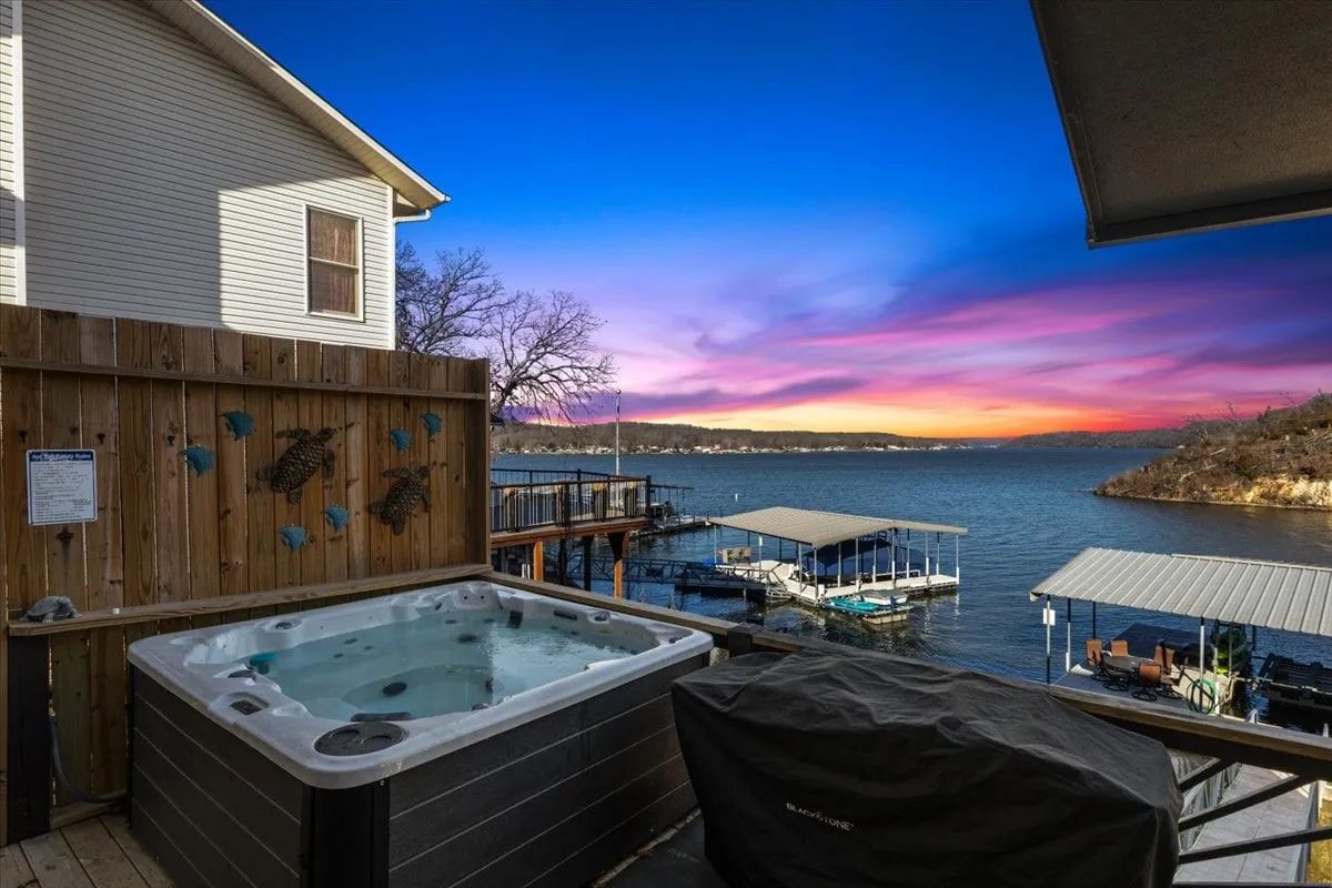 A picturesque view from the hot tub overlooking the lake and dock area at sunset. The scene highlights the serene water, the inviting hot tub, and a sky bathed in soft evening hues, capturing a moment of post-adventure relaxation.
