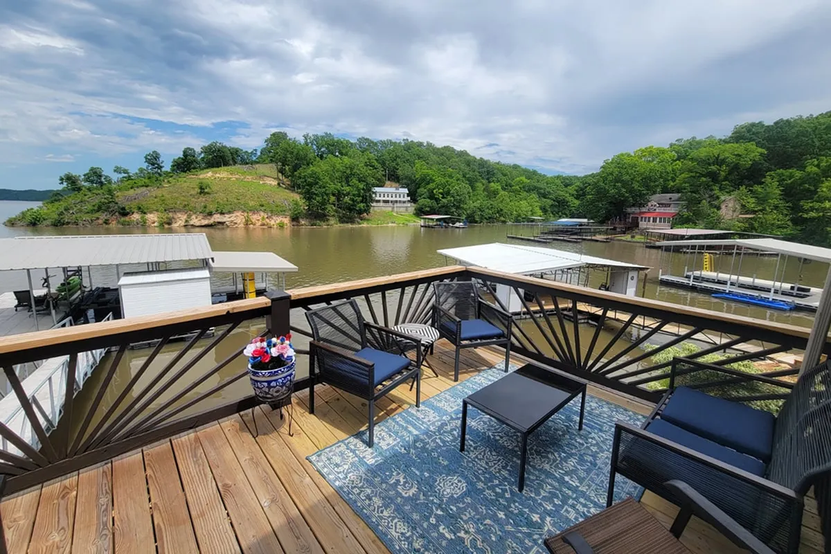 A comfortable seating area on an exterior deck offers panoramic views of the lake. Decorative railings frame the space, inviting guests to relax, socialize, and take in the natural beauty, especially during sunset or under the stars.
