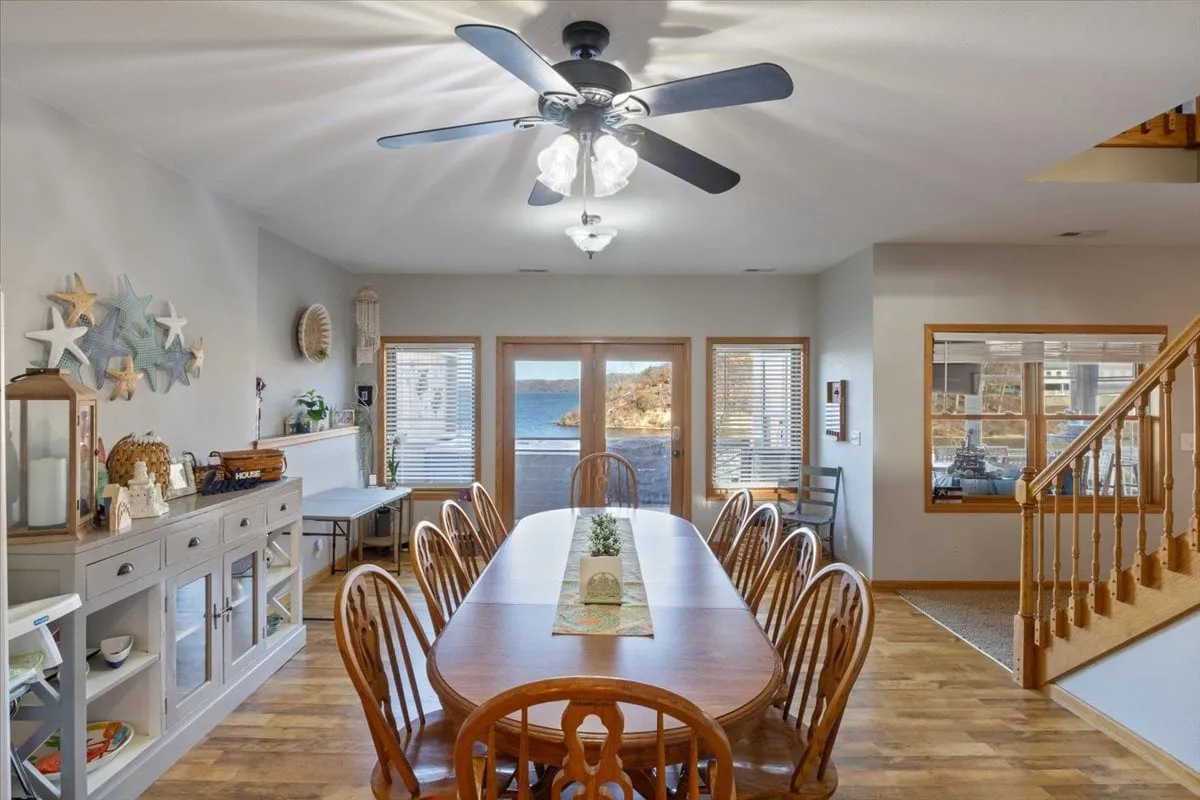 A long wooden dining table set next to large windows offers sweeping views of the lake. The room is warmly lit, with decorative starfish on the wall and a communal feel, perfect for gatherings, meals, or group conversations.