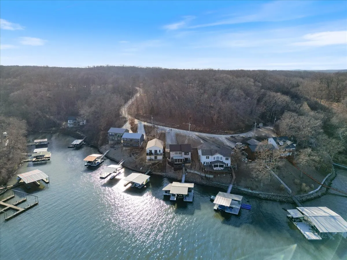 This exterior image showcases a tranquil shoreline at Lake of the Ozarks, with houses and boathouses nestled along the water, a calm lake surface, and a wooded backdrop. The scene evokes the relaxed atmosphere of lakeside living and offers visual cues to outdoor activities like boating, fishing, and picnicking.