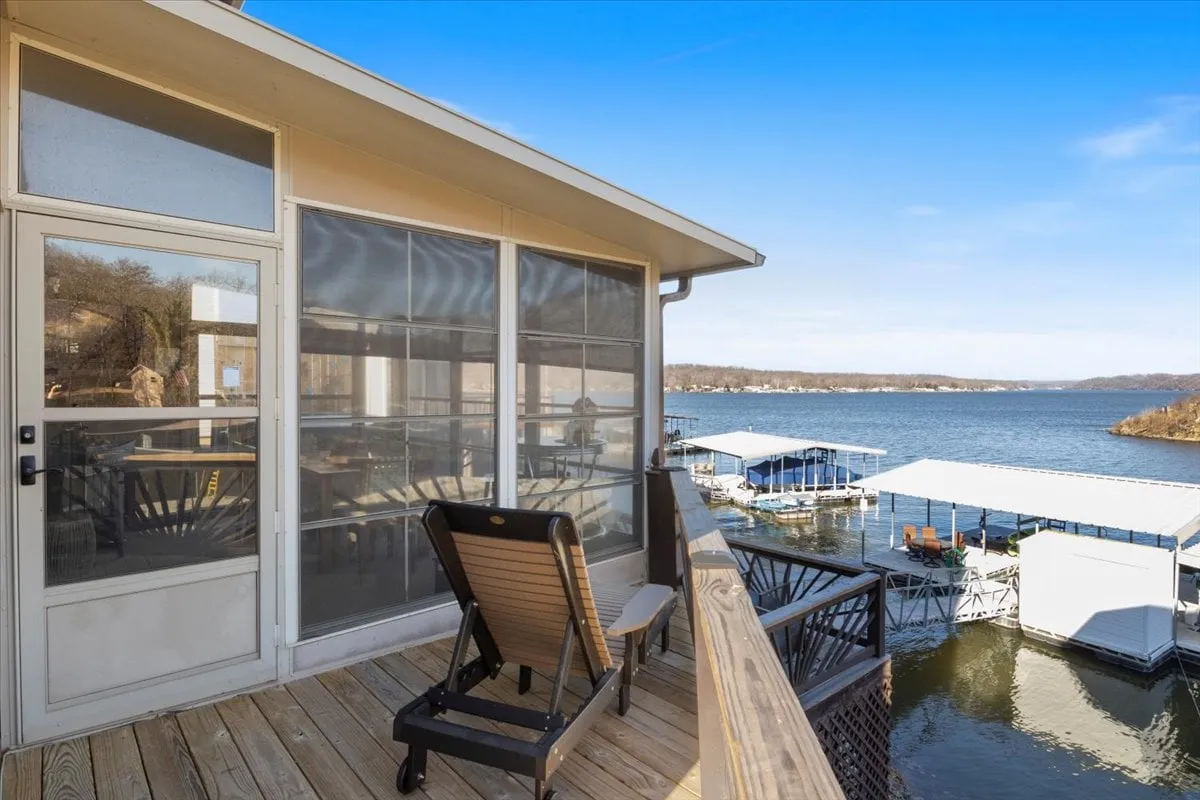 A deck with a lounge chair overlooking the water, with boathouses in the distance. The scene suggests a quiet space for reading, lounging, or enjoying a lakeside breeze.
