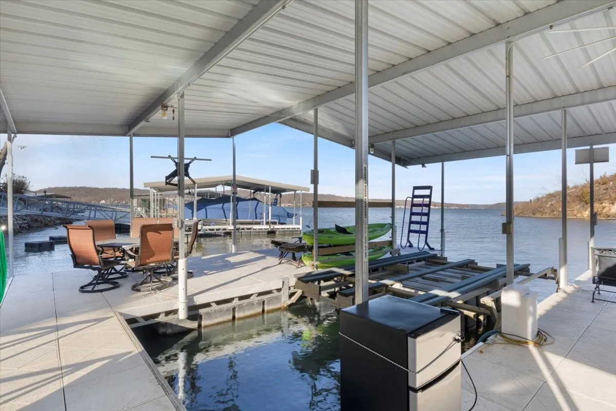 An inviting lakeside setting featuring a dining set on the deck, kayaks ready for adventure, a boat dock, and a tranquil water view. The space is ideal for family meals, water sports, and relaxing outdoor time.